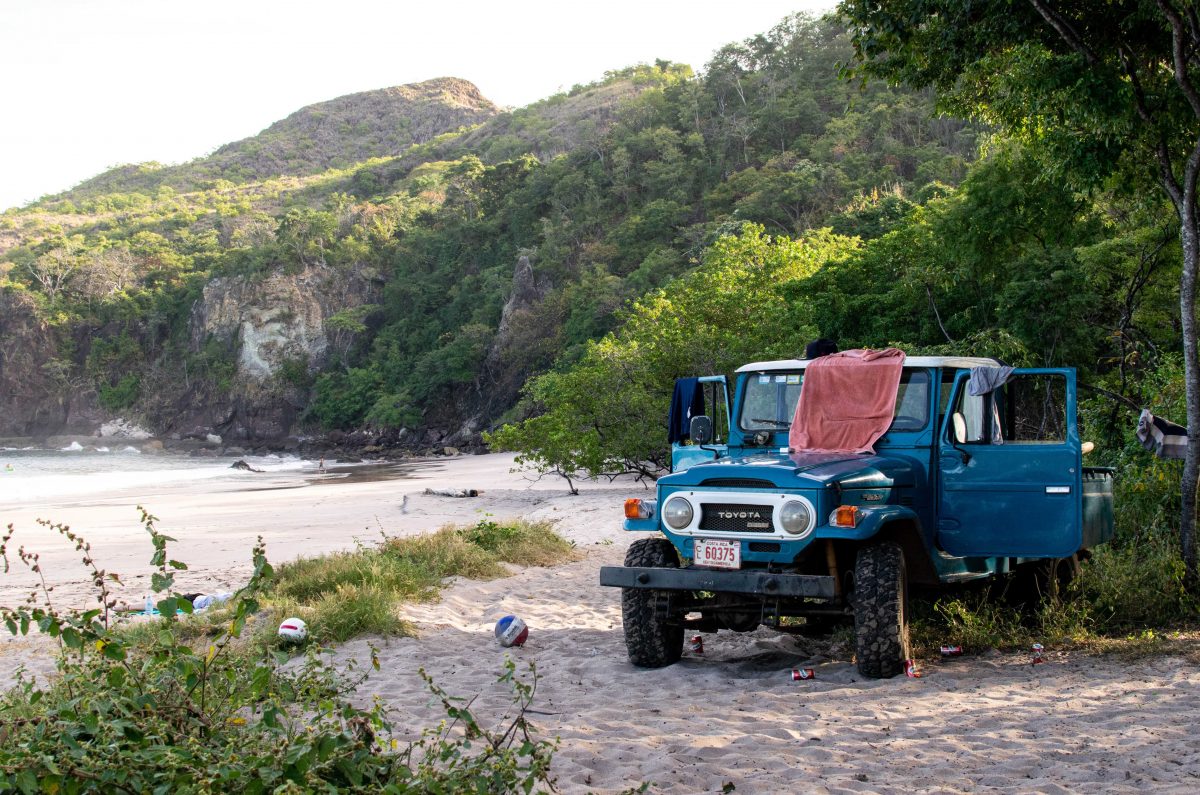 Dreamsea Costa Rica Surf Camp | backpacking, travel, hostel, surf, and yoga camp | Media Files | Lifestyle Image of Surf and Yoga Camp Resort | Retro Toyota Land Cruiser with beach apparel and gear scattered around on an undisclosed location on a beach with mountains in the background in Tamarindo, Costa Rica at Dreamsea Surf Camp