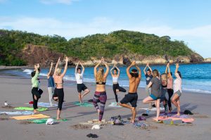 Dreamsea Costa Rica Surf Camp | backpacking, travel, hostel, surf, and yoga camp | Media Files | Lifestyle Image of Surf and Yoga Camp Resort | Group of individuals doing Yoga at Dreamsea Surf and Yoga Camp while on a beach in Tamarindo, Costa Rica with mountains in the background