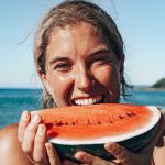 Dreamsea Costa Rica Surf Camp | backpacking, travel, hostel, surf, and yoga camp | Media Files | Lifestyle Image of Surf and Yoga Camp Resort | Girl eating a watermelon on a beach in Tamarindo, Costa Rica at Dreamsea Surf Camp