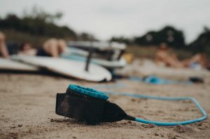 Dreamsea Costa Rica Surf Camp | backpacking, travel, hostel, surf, and yoga camp | Media Files | Lifestyle Image of Surf and Yoga Camp Resort | picture of a surf board blurred in the background with the ankle bracelet shown in focus in the foreground on a beach in Tamarindo, Costa Rica